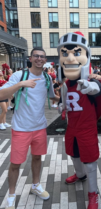 Young man wearing shorts and a T-shirt poses with the Rutgers Scarlet Knight mascot.