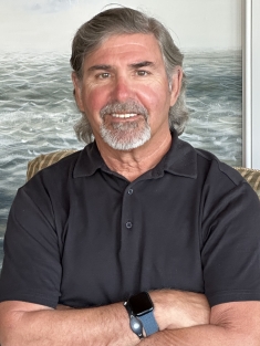Headshot of man with beard wearing a dark polo with his arms crossed in front of him