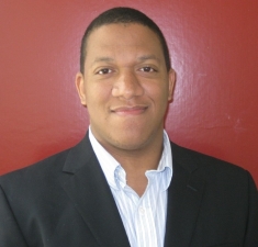 Head shot of Black male with short hair, wearing a black suit jacket and white collared shirt.