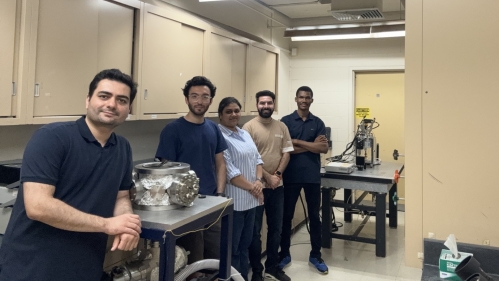 Male professor poses in his labe with four students.