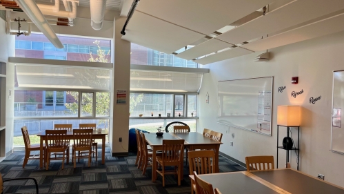 Room with several tables and chairs, a large window, and whiteboards and other accessories