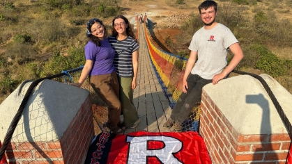 Two femal and one male student standing on a bridge the help build in Africa.