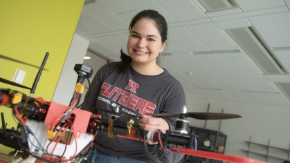 Female student wearing a gray Rutgers Tshirt standing with a drone.