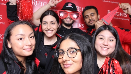 Group of six college students posing in front of Rutgers banner.