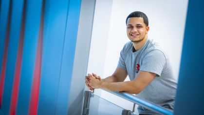 Smiling male student with hands crossed leaning on bannister