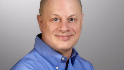 Headshot of white male, bald wearing a blue open collar shirt.