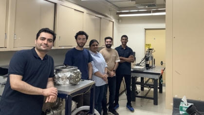 Male professor poses in his labe with four students.