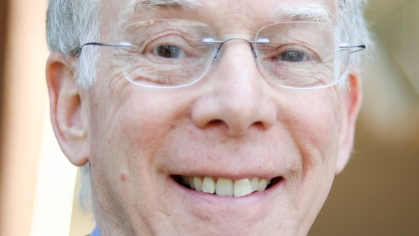 Headshot of male with white hair and glasses, wearing a blue suit, blue shirt and red tie.