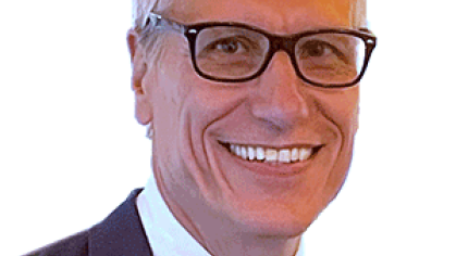 Headshot of male with short grey hair wearing eyeglasses, dark suit, tie and white shirt.