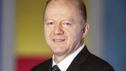 Headshot of a man with close cropped hair wearing a black suit and tie and white shirt.