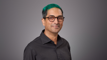Headshot of male with eyeglasses and green hair wearing a black button down shirt