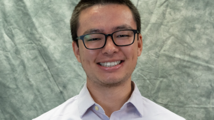 Headshot of Asian male with short black hair, wearing black horn rimmed, and light colored button down shirt. 