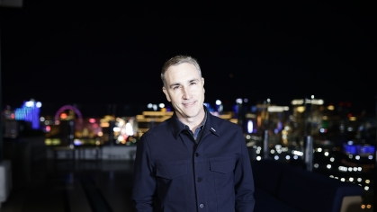 Man standing against a night skyline wearing a dark shirt and smiling.