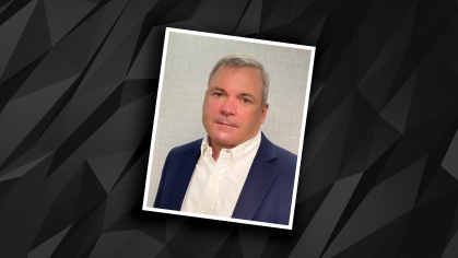 Headshot of male wearing a black suit jacket with white button doen shirt against a black and grey patterned design background.