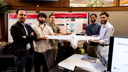 Four male engineering students pose with their professor. They are holding a drone and there is a research poster behind them.