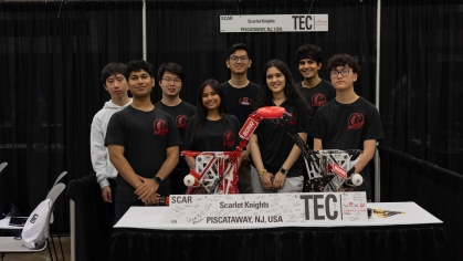 Eight students pose in front of a table with their robotic device.