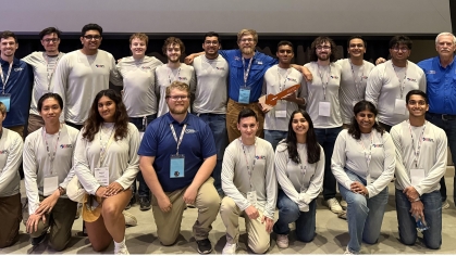 About 25 students pose in two rows, all wearing white tee shirts.