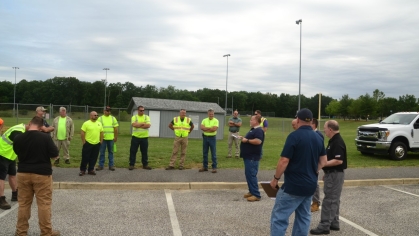 People in yellow vests getting instructions in an outdoor setting.