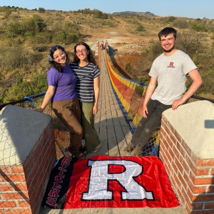 Two femal and one male student standing on a bridge the help build in Africa.