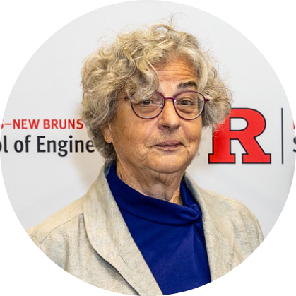 Headshot of woman with short, gray curly hair with glasses. Wearing a dark blue shirt with a beige jacket.