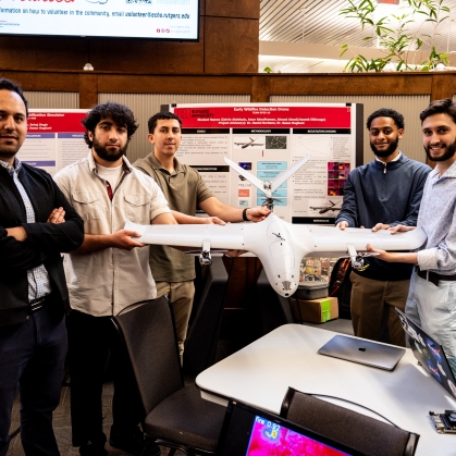 Four male engineering students pose with their professor. They are holding a drone and there is a research poster behind them.