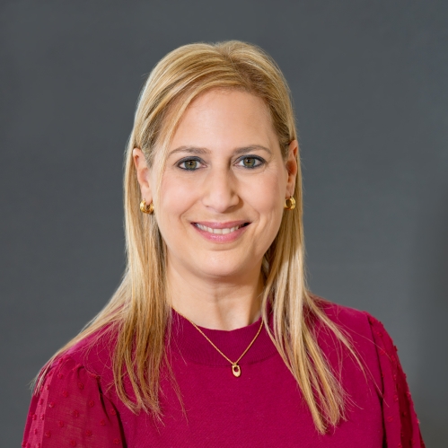Head shot of woman with long blond hair, wearing gold hoop earrings, a gold necklace, and a red pullover sweater.