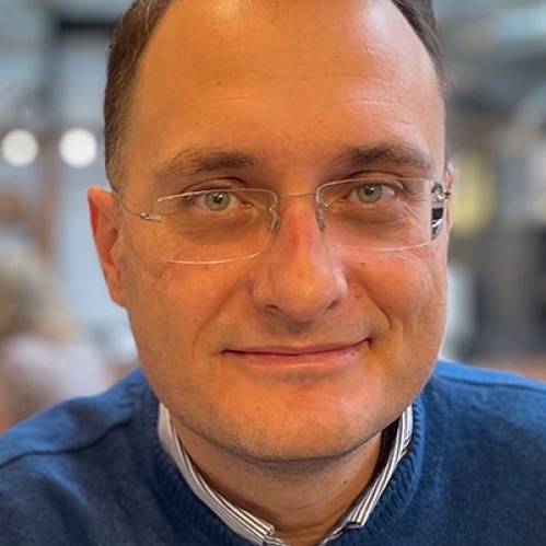 Head shot of male with short brown hair and eyeglasses, wearing a blue pullover sweater.