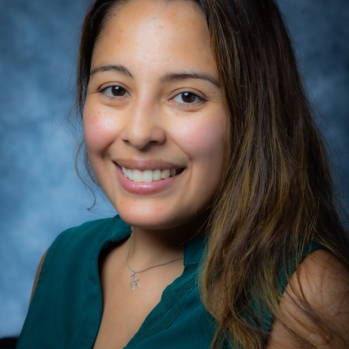 Head shot of female with ong brown hair, wearing a dark green top.