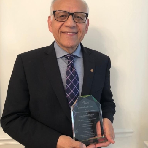 Male with white hair and eyeglasses holds award.