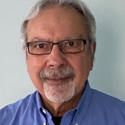 Headshot of male with short, white hair, and facial hair, wearing eyeglasses and a button down blue shirt.