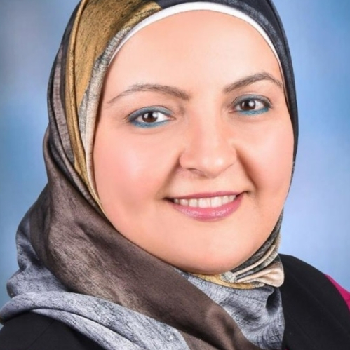 Female wearing a grey and brown head scarf, and a pink and black shirt with a necklace.