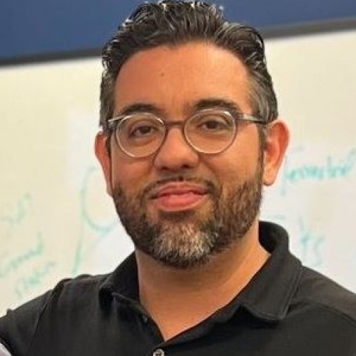 Headshot of male with short hair and facial hair, wearing eyeglasses and a black polo shirt.
