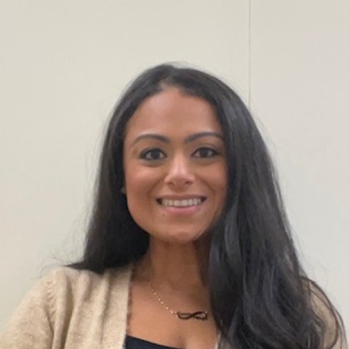 Headshot of female with long black hair, wearing a tan sweater and a black shirt. an