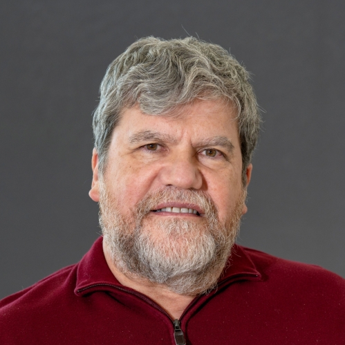 Headshot of male with short, grey hair and facial hair, wearing a burgundy half-zip sweater.