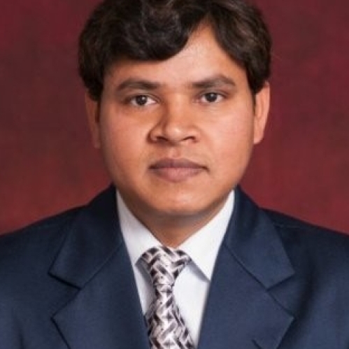 Headshot of male with dark hair, weasring a blue suit, shite shirt, and silver patterned tie.