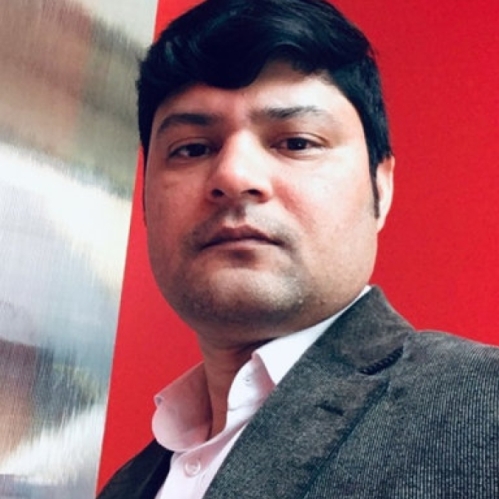Head shot of male with dark short hair, wearing a pink button down shirt with a grey suit jacket.
