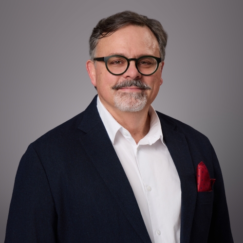 Headshot of male with eyeglasses wearing a white button down shirt a black suit jacket and a red pocket square