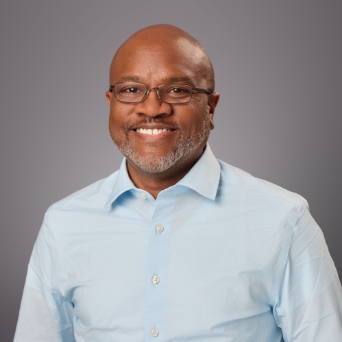 Headshot of smiling black male with eyeglasses wearing a light blue button down shirt.