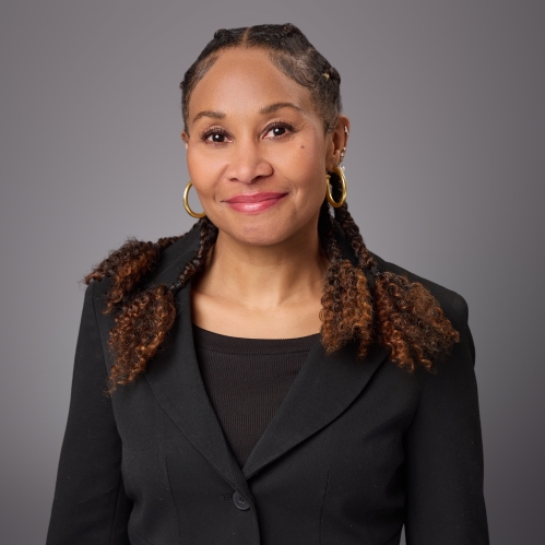 Headshot of black woman with long hair wearing big gold hoop earrings, a black blouse underneath a black jacket.