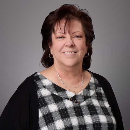 Headhsot  of woman with short brown hair wearing a black and white checkered blouse underneath a black sweater.