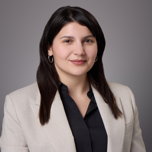 Headshot of female with long black hair, wearing a black blouse beneath a tan jacket.