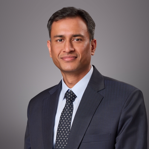 Headshot of male wearing a dark blue suit, light blue shirt, and dark blue tie.