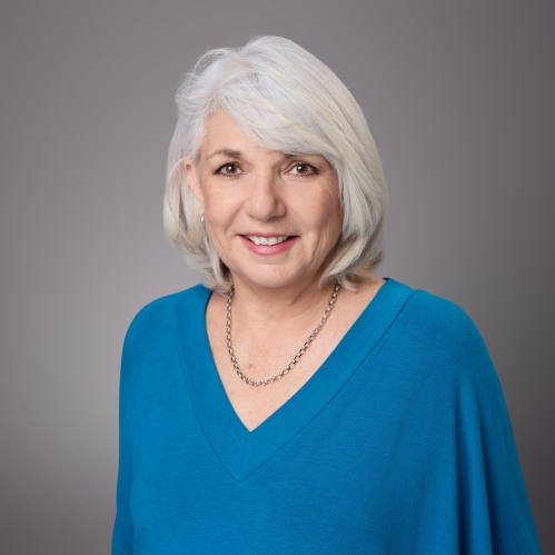 Headshot of woman with grey hair and a v neck blue pullover.