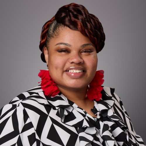 Headshot of black woman with long red earrings wearing a black and white patterned shirt.