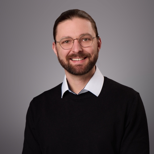 Headshot of male with hair pulled back, beard, moustache and eyeglasses.
