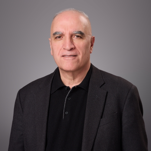 Headshot of male with white hair wearing a black sweater underneath a black suit jacket.