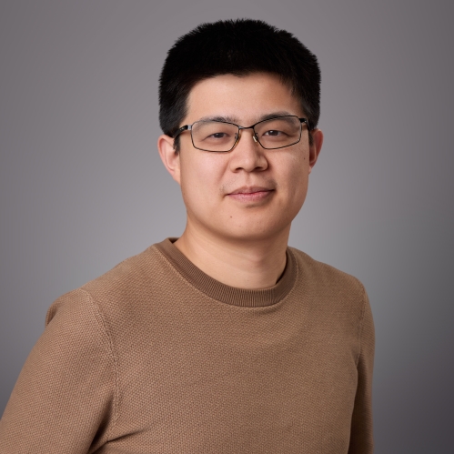 Headshot of male with short black hair and eyeglasses wearing a brown sweater.