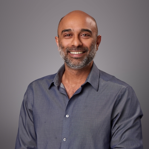 Headshot of bald male with sruffy beard wearing a bluish grey button down shirt.