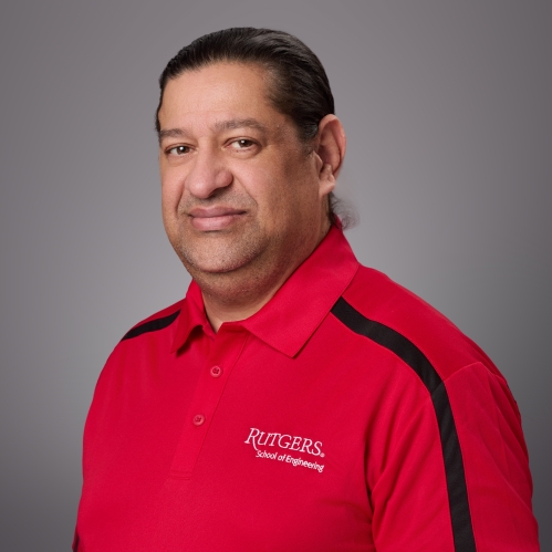 Headshot of male with dark brown hair pulled into a ponytail wearing a red Rutgers polo shirt.