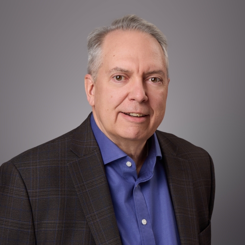 Headsot of male with grey hair wearing adark blue button down shirt and a black suit jacket.